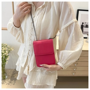 Close-up of bright pink leather phone bag with chain strap against white dress