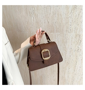 Close-up of a brown leather crossbody bag with a distinctive gold woven metal buckle detail