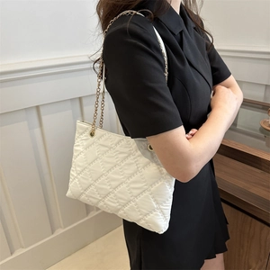 White quilted tote bag with gold chain strap shown on model in a minimalist setting