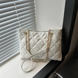 Stylish white quilted tote bag with golden chain straps shown on a windowsill