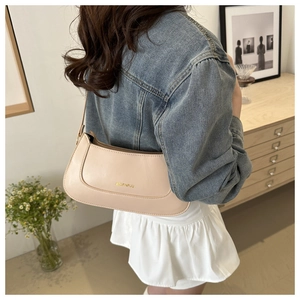 Detail showing the beige moon-shaped shoulder bag with gold branding in a home setting