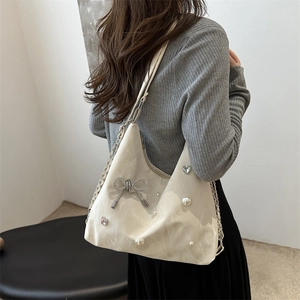 Elegant cream tote bag with pearl bow and silver chain strap worn by a model