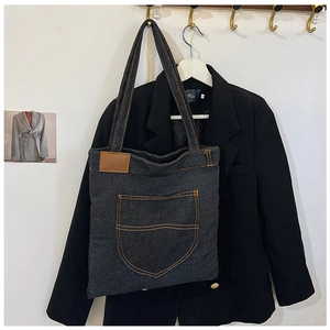 Λεπτομέρεια από σκούρα γκρι τσάντα denim με πορτοκαλί ραφές και δερμάτινο σήμα