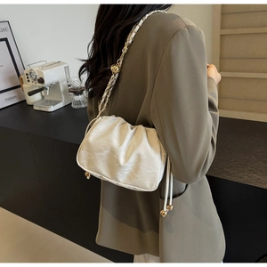 Detail of white pleated cloud bag with metallic chain strap worn as a crossbody