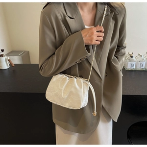 Detail of a creamy white pleated drawstring bag with a gold chain strap on a model