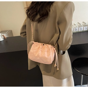 Pink drawstring bucket bag with gold chain strap shown on person in lifestyle setting