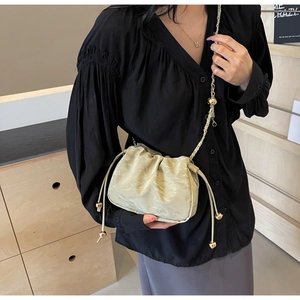Close-up of light green pleated crossbody bag with drawstring and gold metal ball detail