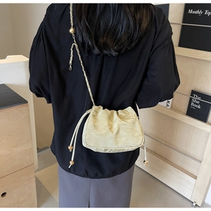 Detail of beige pleated cloud bag with gold ball drawstring and chain strap on shoulder