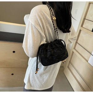 Close-up of black pleated cloud bag with gold chain strap and decorative golden bead