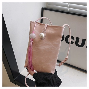 Close-up of pink crossbody bag with pearl button, tassel detail and pleated texture