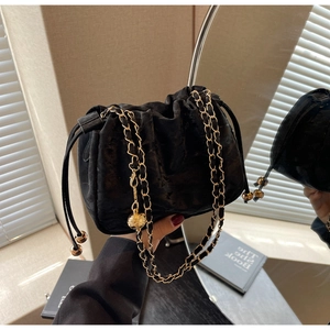Close-up of black velvet bucket bag with gold chain and quilted metal sphere adjuster