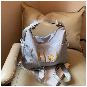 Detail of light gray nylon bag featuring yellow Hai embroidery and side drawstring pocket