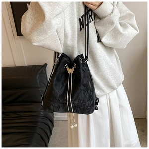 Detail of a black drawstring bucket bag with metal butterfly and pearl pendant charms