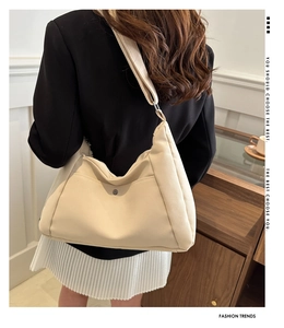 Detail of cream crescent shoulder bag featuring wide strap and metallic buckle accent