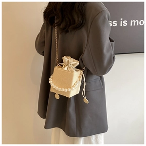 Detail of cream woven mini bucket bag featuring a pearl handle and gold chain strap