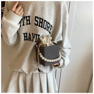 Detail of grey bucket bag featuring pearl handle and gold chain strap on street model