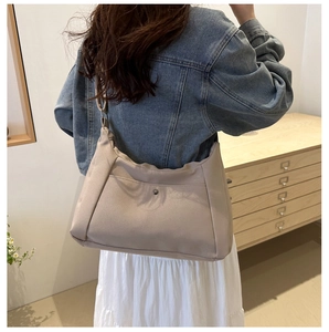 Détail du sac hobo en nylon beige montrant la poche avant et la finition métallique chic