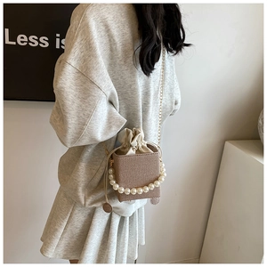 Detail of woven khaki bucket bag featuring pearl handle and golden chain strap