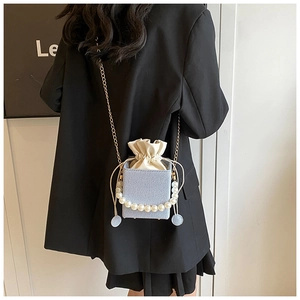 Detail of light blue crossbody bucket bag with pearl handle and golden chain strap