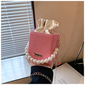 Detail view of pink woven bucket bag featuring pearl handle and golden chain strap