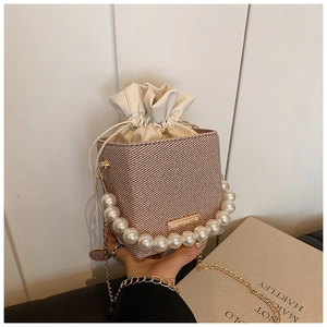 Detail of light khaki woven bucket bag featuring pearl handle and gold chain strap