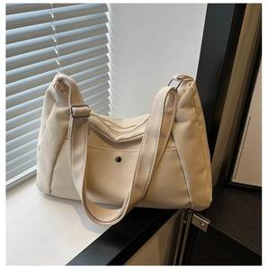 Detail of cream canvas tote showing adjustable wide strap and metallic snap-button pocket