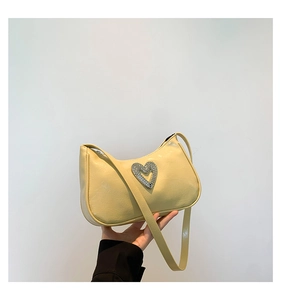 Detail of beige patent leather bag featuring a heart-shaped rhinestone buckle and strap