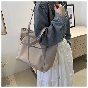 Gros plan sur le sac cabas en toile beige avec poche avant à rabat et bouton argenté