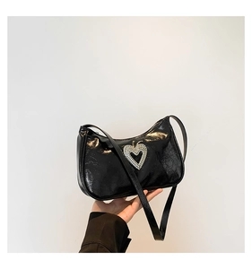 Close-up of a black patent leather shoulder bag featuring a large silver rhinestone heart