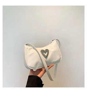 Close-up of white glossy shoulder bag featuring a heart-shaped rhinestone buckle detail