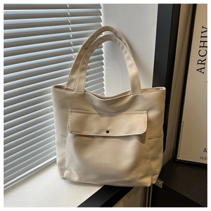 Détail du sac cabas minimaliste en toile beige avec poche à rabat et bouton en métal rétro