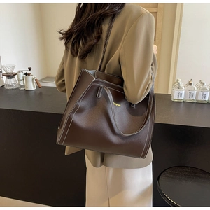 Detail of dark brown tote bag with white contrast stitching and gold lettering logo