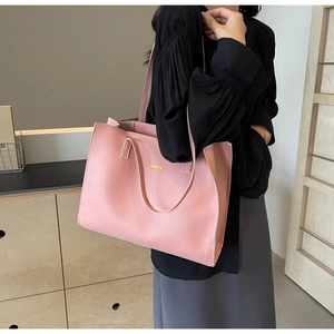 Detailed close-up of a pink matte leather tote bag with a golden brand logo on its side