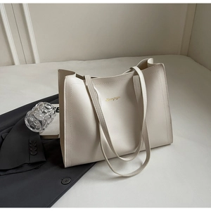 Macro view of cream leather tote bag featuring gold logo and minimalist shoulder straps