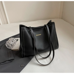 Detail of black leather tote bag with white contrast stitching and gold branding