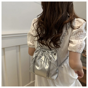 Détail du sac seau argenté avec texture métallique et cordon sur une robe blanche