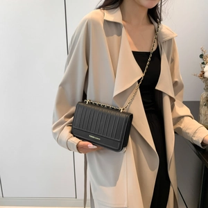 Sac à bandoulière noir texturé à rayures avec chaîne dorée porté sur manteau beige