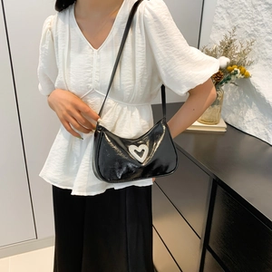 Glossy black patent leather underarm bag with a large rhinestone heart on white outfit