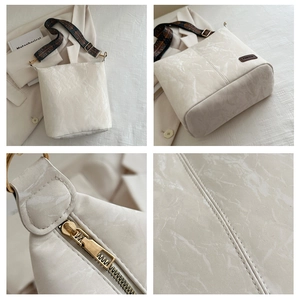 Detail of white marble texture leather bag with patterned strap and golden hardware
