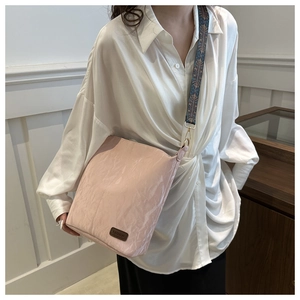 Detail of light pink textured shoulder bag featuring fashion patch and geometric strap