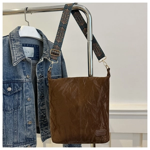 Close-up of brown crinkled shoulder bag featuring a retro chic pattern wide strap