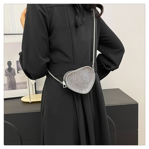 Detail of silver sequin heart-shaped crossbody bag with metallic chain on black dress