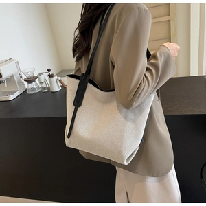 Minimalistische beige Canvas-Tasche mit schwarzen Lederriemen an der Schulter eines Models