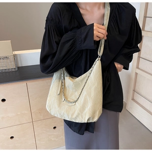 Detail of beige pleated tote bag with silver chain and wide shoulder strap shown on model