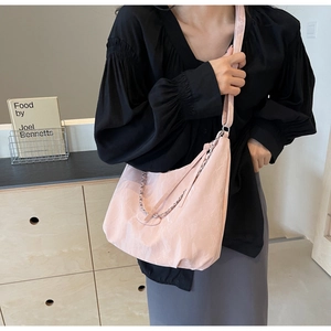 Detail of light pink tote bag featuring a decorative silver chain and wide shoulder strap