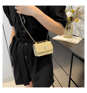 Dettaglio mini borsa in paglia beige con catena dorata su vestito nero