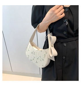 Detail of woven beige handbag with green floral embroidery and a large leather bow