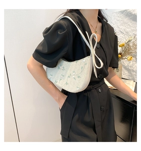 Detail of woven crescent bag with floral embroidery and oversized bow on shoulder strap