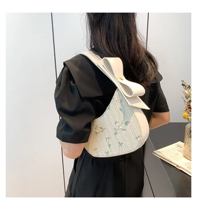 Detail of white half-moon bag with floral embroidery and oversized leather bow strap