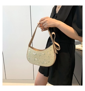 Detail of light green crescent straw bag with floral embroidery and large bow strap